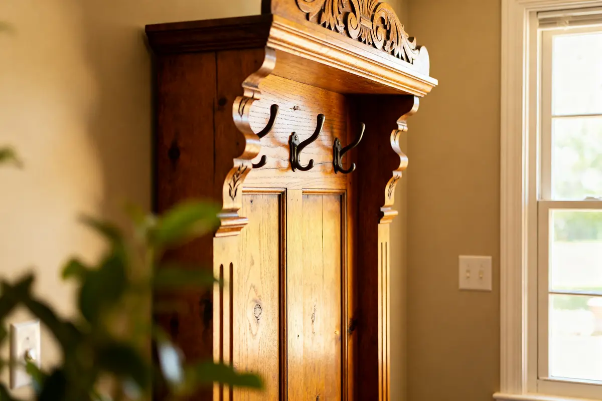 Ornate antique hall tree with hooks next to a sunlit window in a cozy room