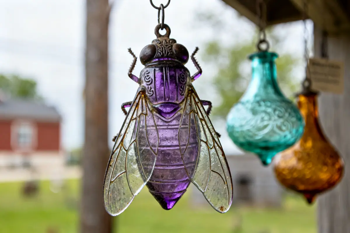 Purple antique glass fly catcher hanging outdoors with colorful glass shapes in background