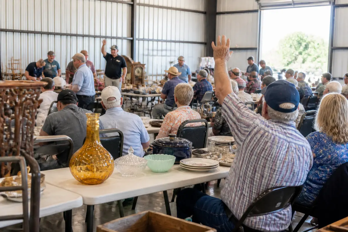 People bidding at the Crestview auction with antiques on display in a large warehouse