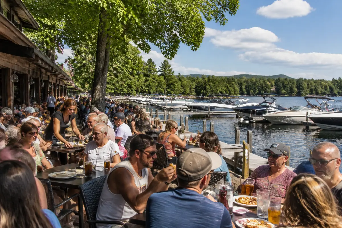 People dining outdoors with lake view, boats, and tree shade at Mug Shotz cafe patio
